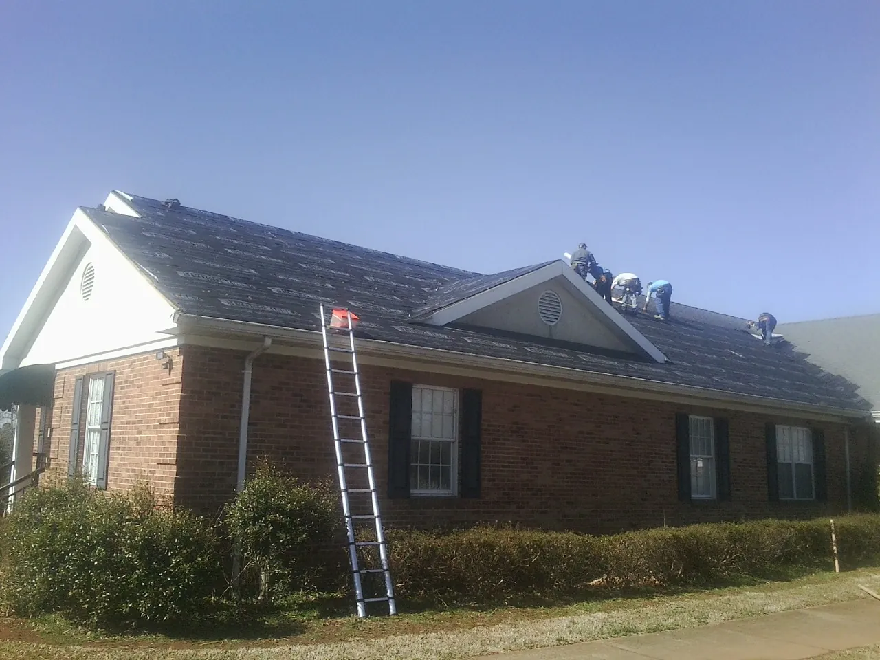 Crew tearing shingles off a brick ranch roof with a ladder set — Emergency Roof Repair work by our crew in Red Cliff