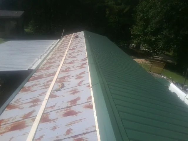 Old rusted panels beside newly installed green metal roofing — Wind Damage Roof Repair by Roofing Brothers in Red Cliff