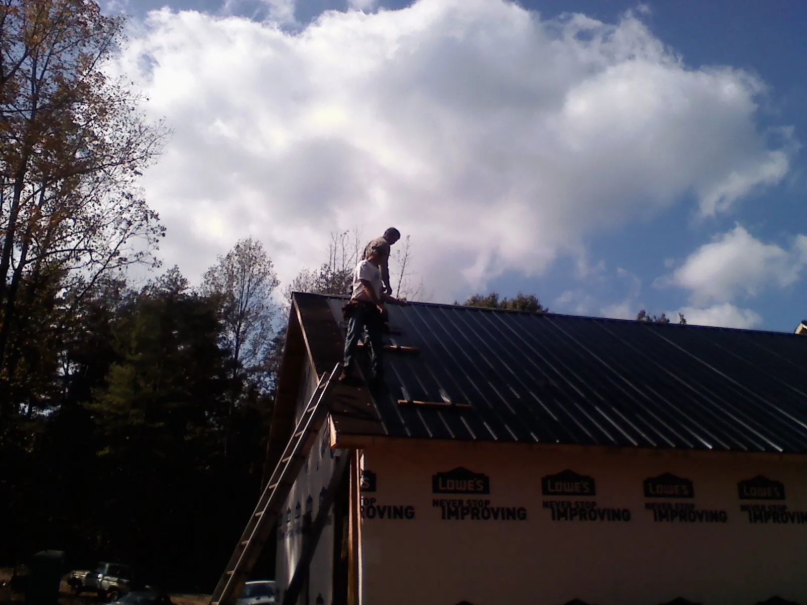Roofer fastening dark metal panels high against a cloudy sky, from a Roof Inspection job in Red Cliff